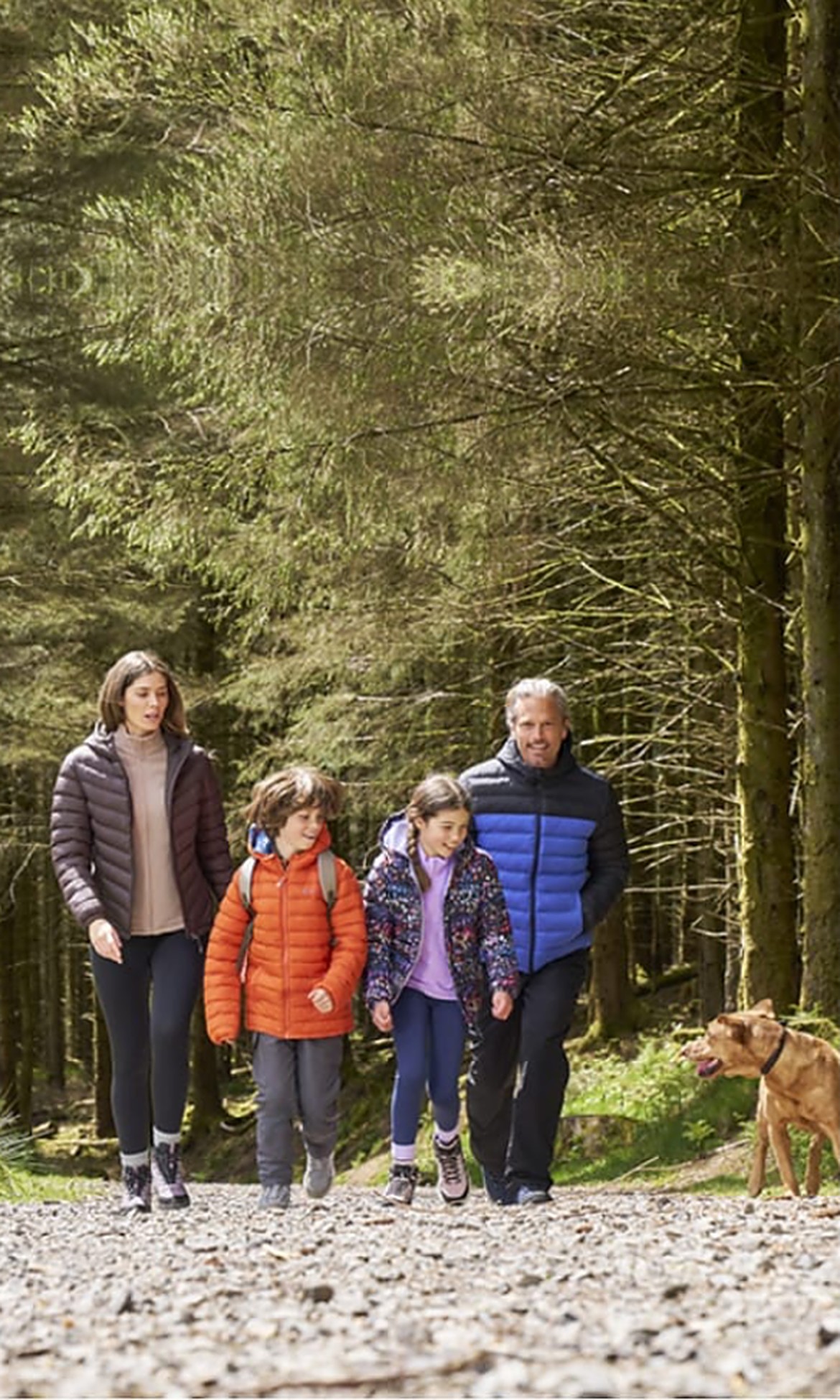 Family with two children and a dog walking a forest trail in outdoor puffer jackets